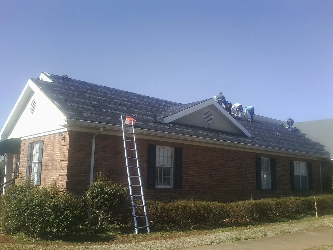 Crew tearing shingles off a brick ranch roof with a ladder set — Metal Roof Repair work by our crew in White Oak
