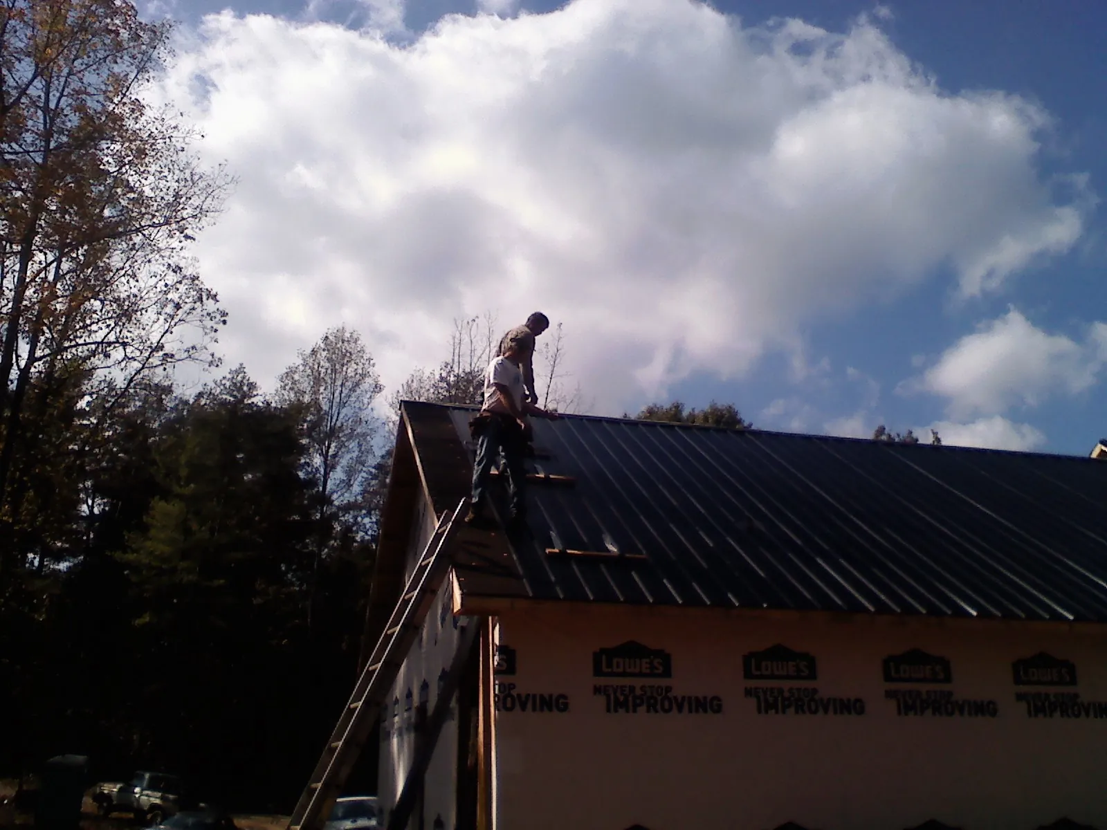 Roofer fastening dark metal panels high against a cloudy sky, from a Roof Inspection job in White Oak