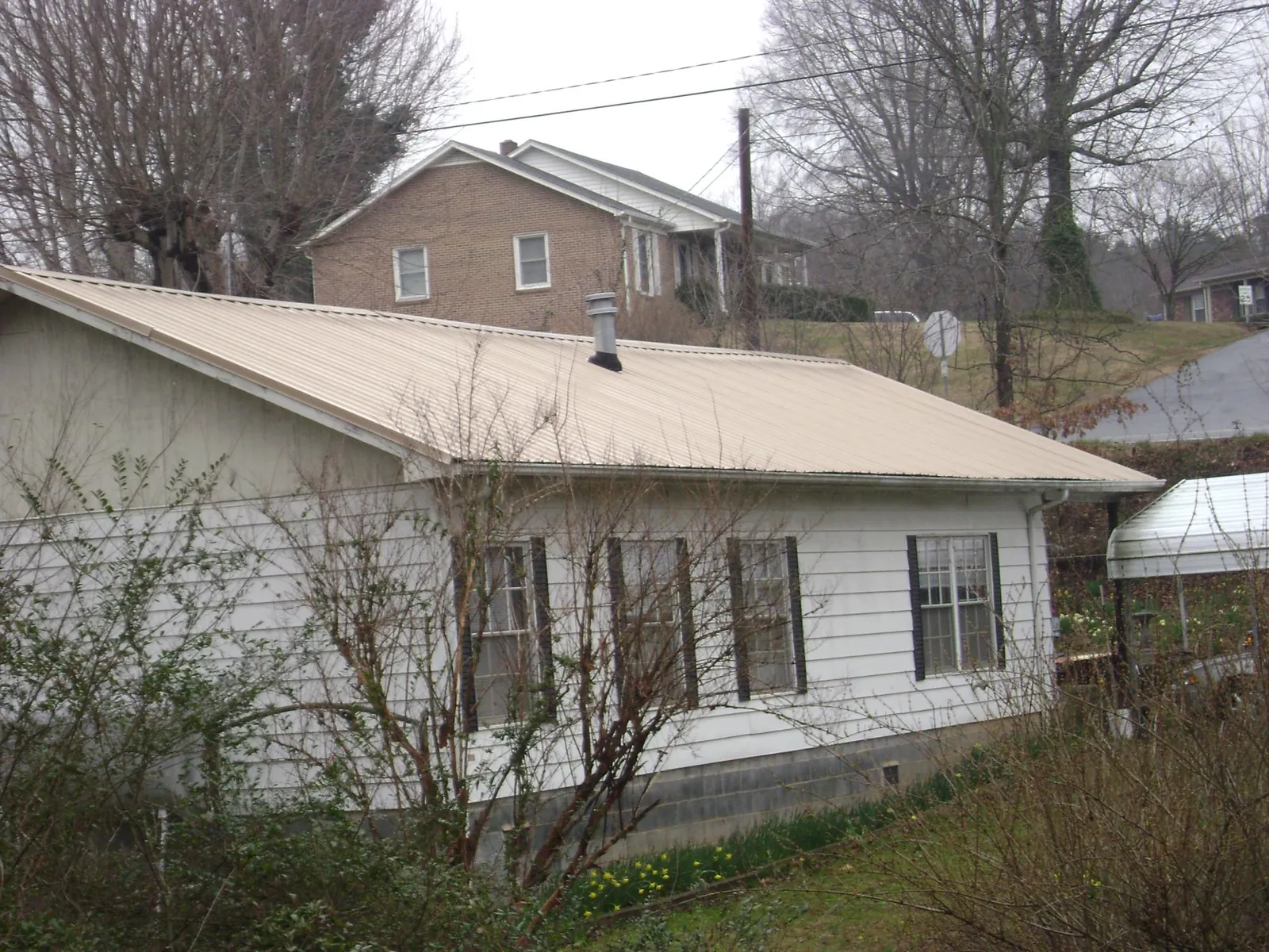 Tan metal roof on a white sided house set into a hillside — Commercial Roofing by Roofing Brothers in White Oak